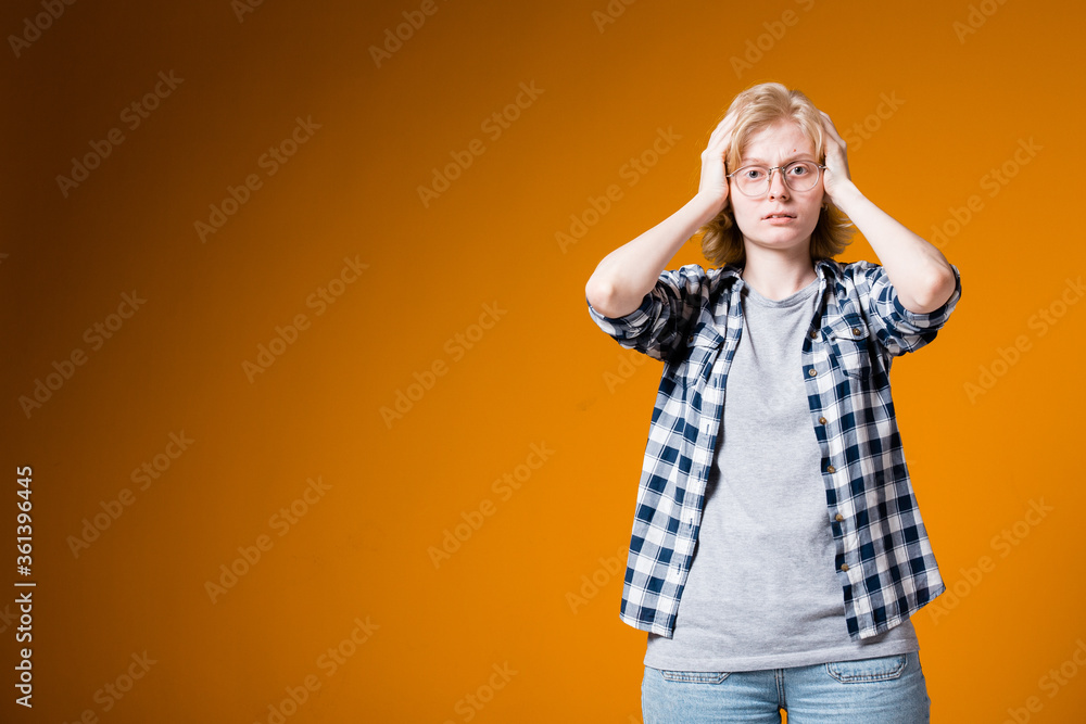 The girl tensely holds his hands behind his head and looking at the camera. Girl with stress on an orange background. The girl tensely holds his hands behind his head and looking at the camera. Girl with stress on an orange background.