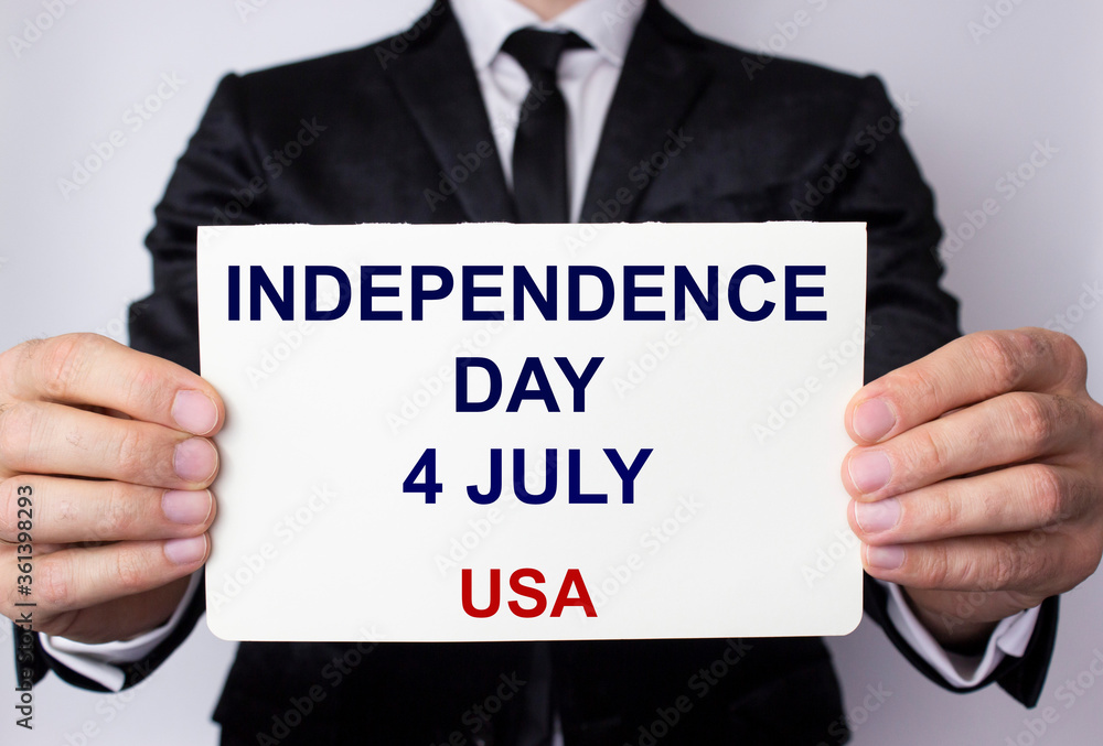 Independence Day 4th of July, an inscription on a white sheet of paper in the hands of a young man in a business suit. USA. Independence Day 4th of July, an inscription on a white sheet of paper in the hands of a young man in a business suit. USA.