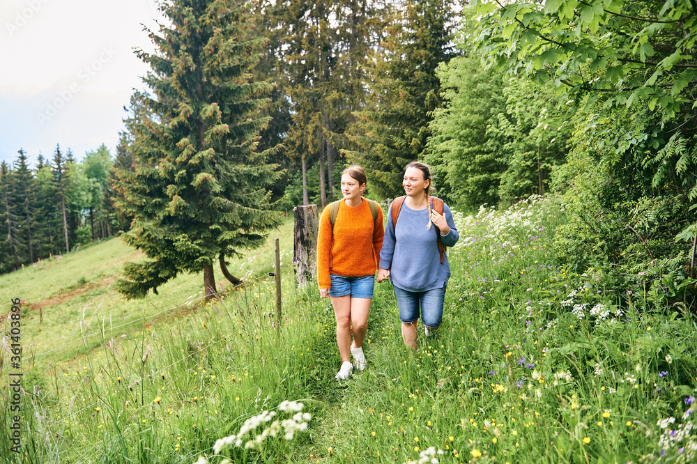 Mother and teenage daughter hiking in green forest, active family time