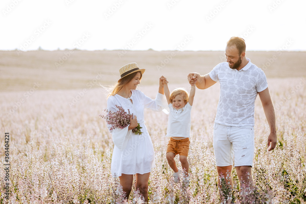 Fototapeta premium Happy family portrait outdoor at the sunset time. People having fun on the field. Concept of friendly family and of summer vacation. Parents and son spending good time. White dress. Straw hat.