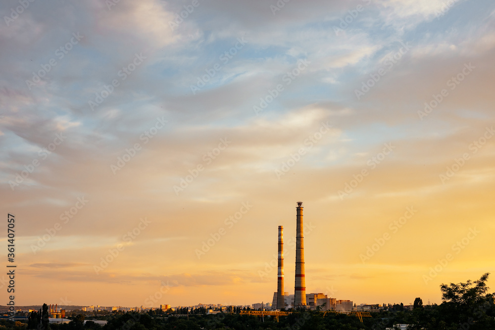 City during warm sunset. Industrial landscape with a thermal power plant in the city at sunrise. Pipe heating system with white steam against the blue sky.