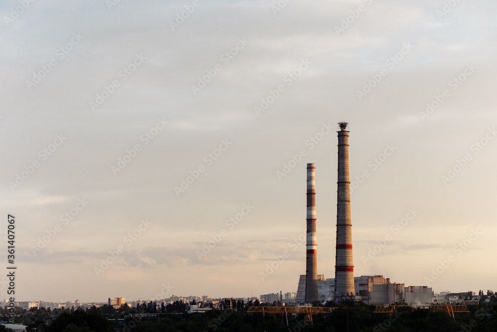 City during warm sunset. Industrial landscape with a thermal power plant in the city at sunrise. Pipe heating system with white steam against the blue sky. City during warm sunset. Industrial landscape with a thermal power plant in the city at sunrise. Pipe heating system with white steam against the blue sky.