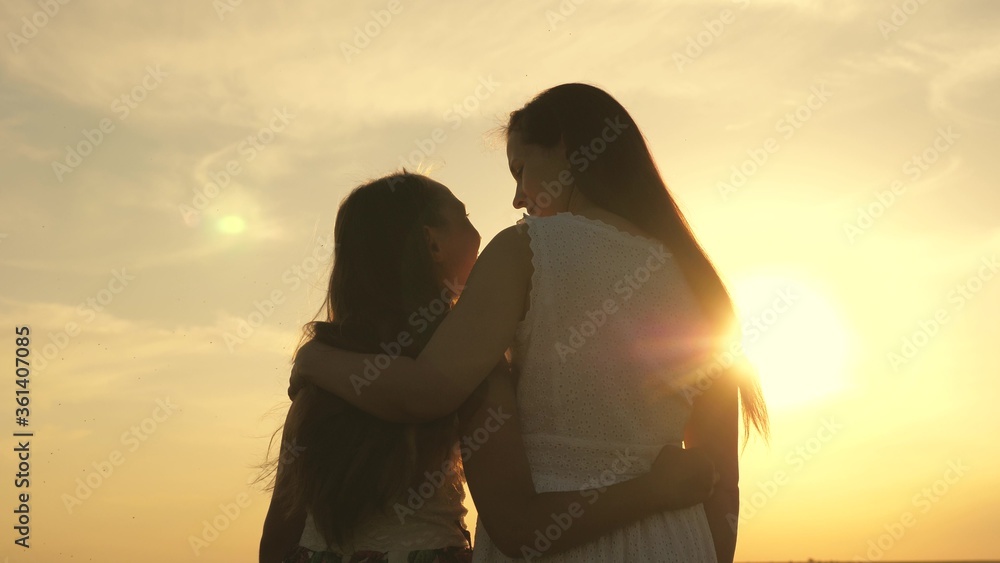 Happy family mom and daughter in field at sunset. Mom hugs daughter, they admire beautiful sunset. concept of happy family of children and children. mother and baby walk in park, field, in sun