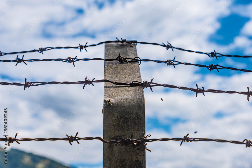 Stacheldrahtzaun und Metallpfosten vor bewölktem Himmel Stacheldrahtzaun und Metallpfosten vor bewölktem Himmel