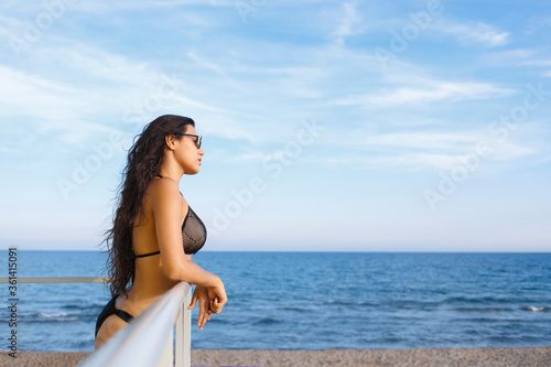 Portrait of a young dreamy women with sexy body enjoying sea landscape while sunbathing on the beach  thoughtful Lain female in bikini resting after swimming on the ocean during her recreation time