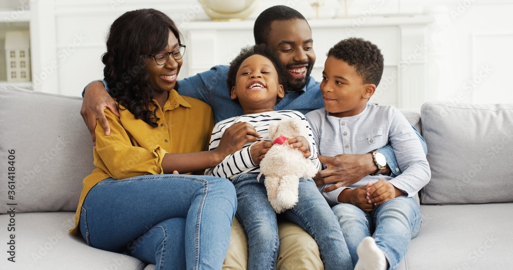 Portrait of African American parents with little kids resting on sofa at home.