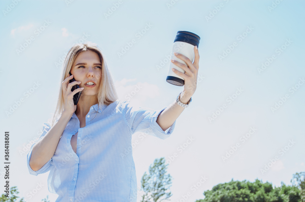 Business lady talks on the phone. A young business woman is working with a laptop in a blue shirt on the street in a Park under the sun! Business concept Business lady talks on the phone. A young business woman is working with a laptop in a blue shirt on the street in a Park under the sun! Business concept