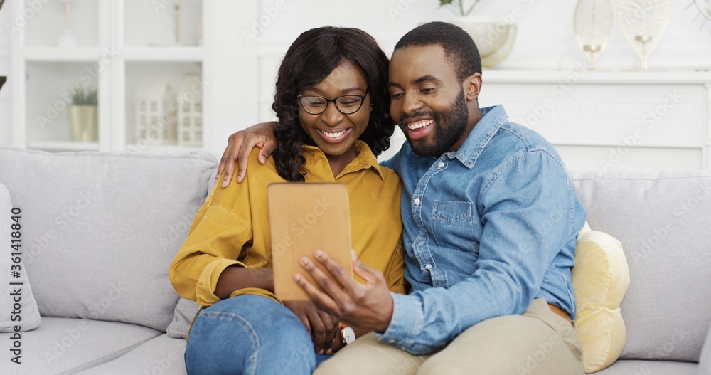 Happy African American couple husband and wife sitting on sofa using tablet at home. Happy African American couple husband and wife sitting on sofa using tablet at home.