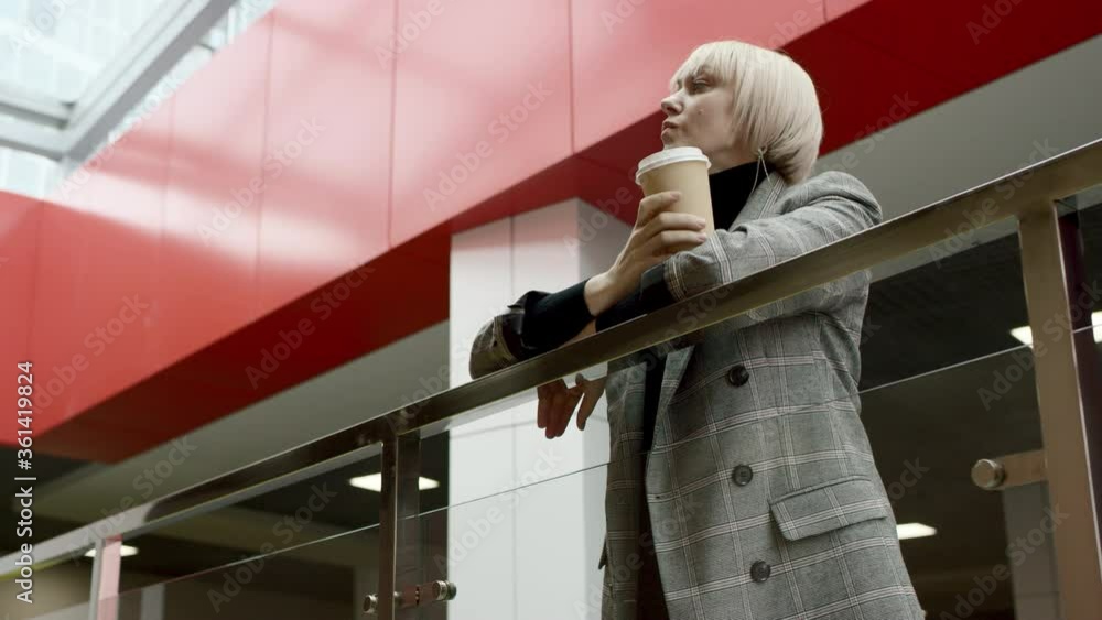 A side view slow motion close up of a blonde business woman leaning on a rail and drinking coffee during lunch A side view slow motion close up of a blonde business woman leaning on a rail and drinking coffee during lunch