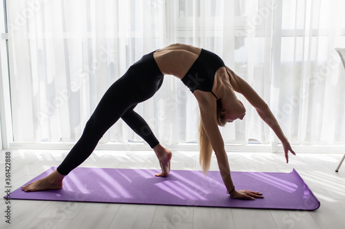 Young sporty attractive woman practicing yoga, doing Mermaid exercise, Eka Pada Rajakapotasana pose, working out, wearing sportswear, pants and top.