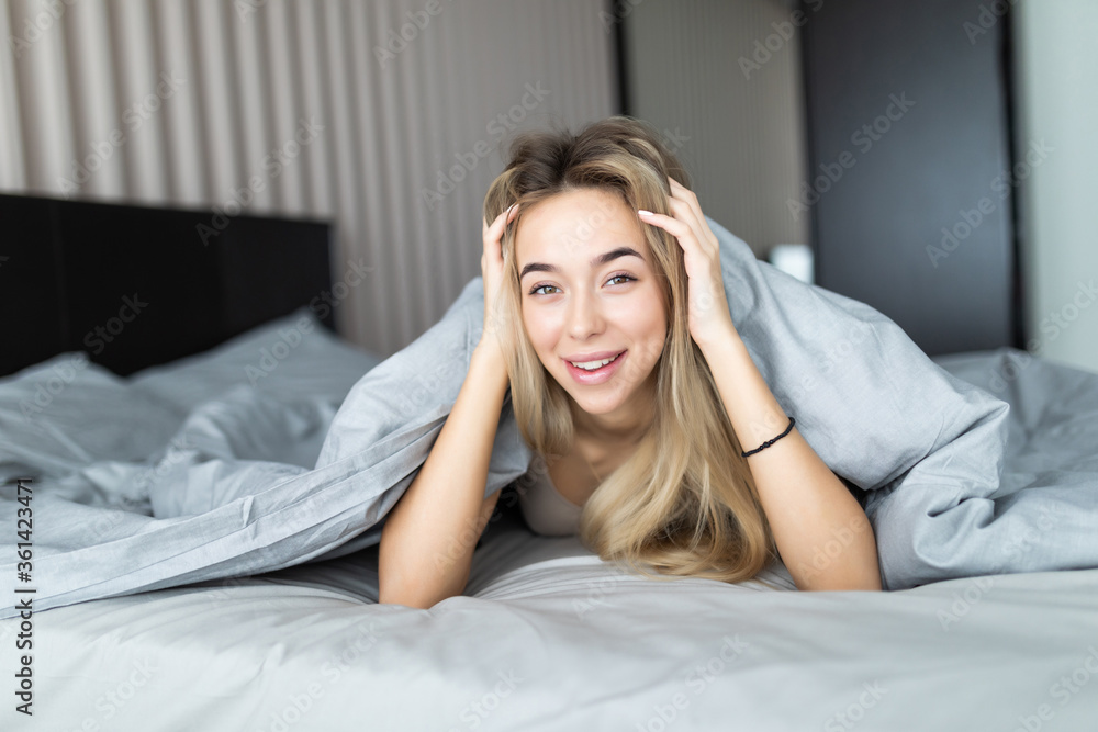Smiling woman under a duvet in her bedroom. Closeup portrait of a beautiful young woman under the blanket. happy good morning Smiling woman under a duvet in her bedroom. Closeup portrait of a beautiful young woman under the blanket. happy good morning