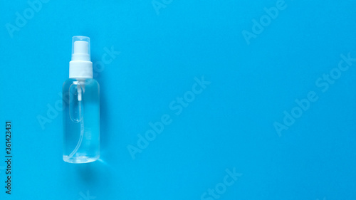 Hand sanitizer transparent bottle with spray cap at the left of blue background. Simple flat lay with copy space. Pastel paper texture. Medical concept. Stock photo.