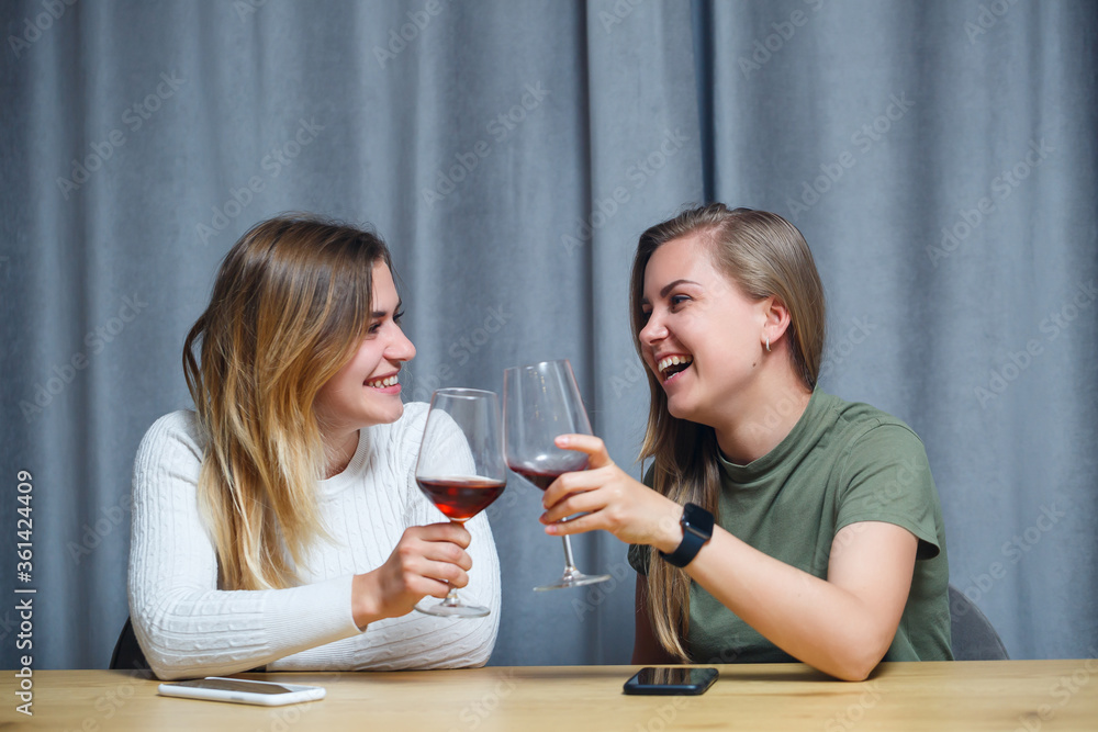 two girls of European appearance with blond hair are sitting at the table, drinking wine and laughing, relaxing at home, alcohol two girls of European appearance with blond hair are sitting at the table, drinking wine and laughing, relaxing at home, alcohol
