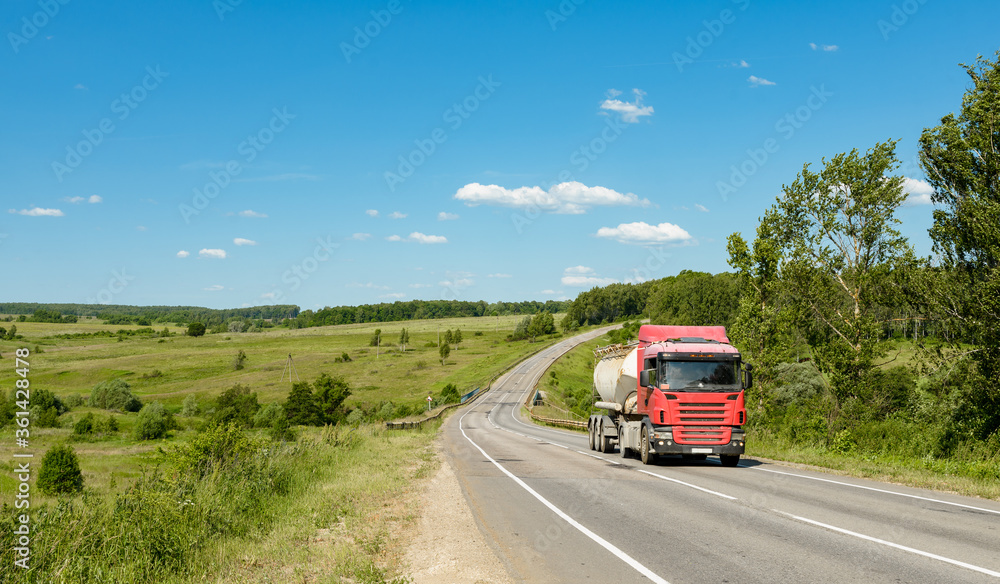 A truck with a tank on the road through the field on a sunny day. A truck with a tank on the road through the field on a sunny day.