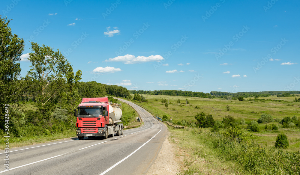 A truck with a tank on the road through the field on a sunny day. A truck with a tank on the road through the field on a sunny day.