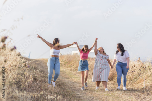 happy friends walk holding hands and arms raised in a meadow