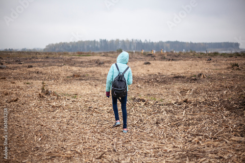 A girl walks across the field. Cut down forest.