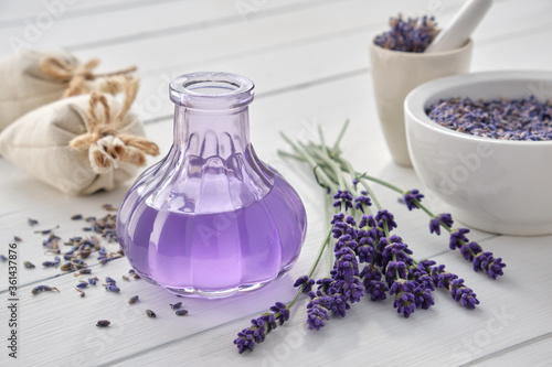 Dry lavender flowers, bottle of essential oil or flavored water, sachet and mortar on white wooden table.