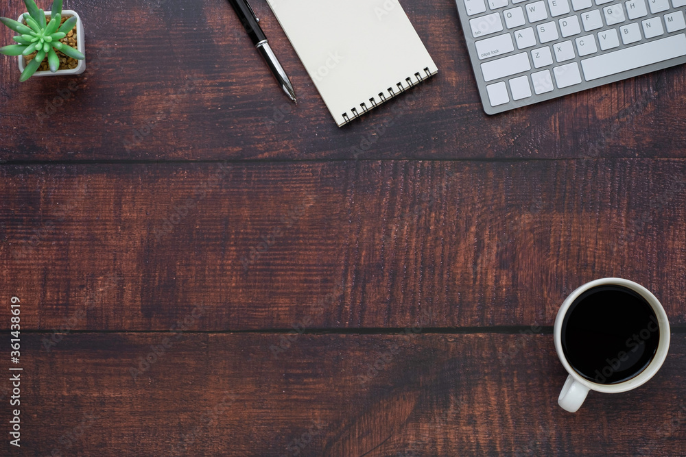Top view above of dark wooden office desk table with keyboard, notebook and coffee cup with equipment other office supplies. Top view above of dark wooden office desk table with keyboard, notebook and coffee cup with equipment other office supplies.