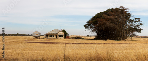 Panoramic image of an old timber worn out abandoned traditional Australian farm house in the middle of a newly harvested field on a agricultural property in rural Victoria, Australia