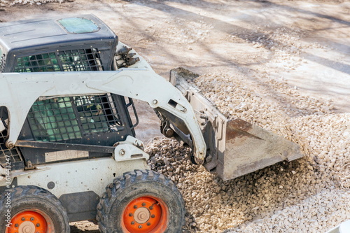 Russia Samara April 2020: Utility tractor Mini loader Bobcat S175 rakes gravel during repair of asphalt on a city street.