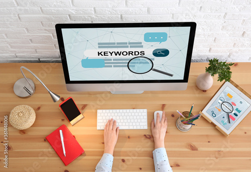 Woman searching keywords with computer at wooden table, top view photo