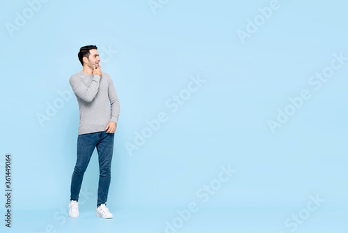 Handsome caucasian man thinking and looking to empty space sideways with hand on chin isolated on light blue background
