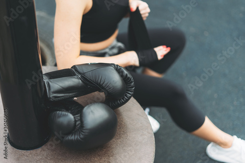 Black leather boxing gloves on the background of athletic girl shakes boxing bandages on the hands before training