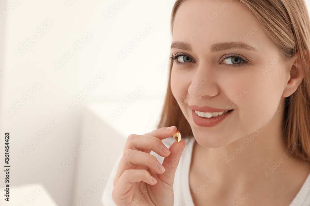 Young woman taking vitamin capsule on light background. Space for text Young woman taking vitamin capsule on light background. Space for text