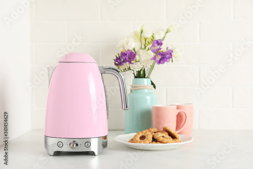 Modern electric kettle, bouquet, cookies and cups on counter in kitchen