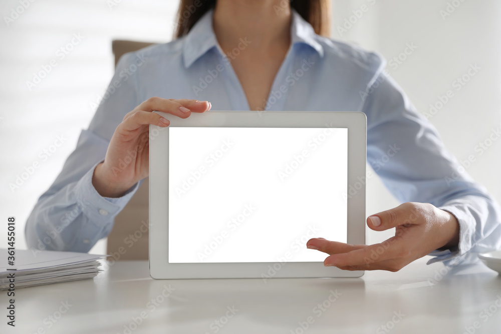 Businesswoman holding modern tablet with blank screen at white table in office, closeup Businesswoman holding modern tablet with blank screen at white table in office, closeup