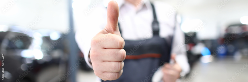 Close-up of mans hand showing thumb-up for well done work. Special garage uniform and work gloves. Restoration workshop and professional service station concept Close-up of mans hand showing thumb-up for well done work. Special garage uniform and work gloves. Restoration workshop and professional service station concept