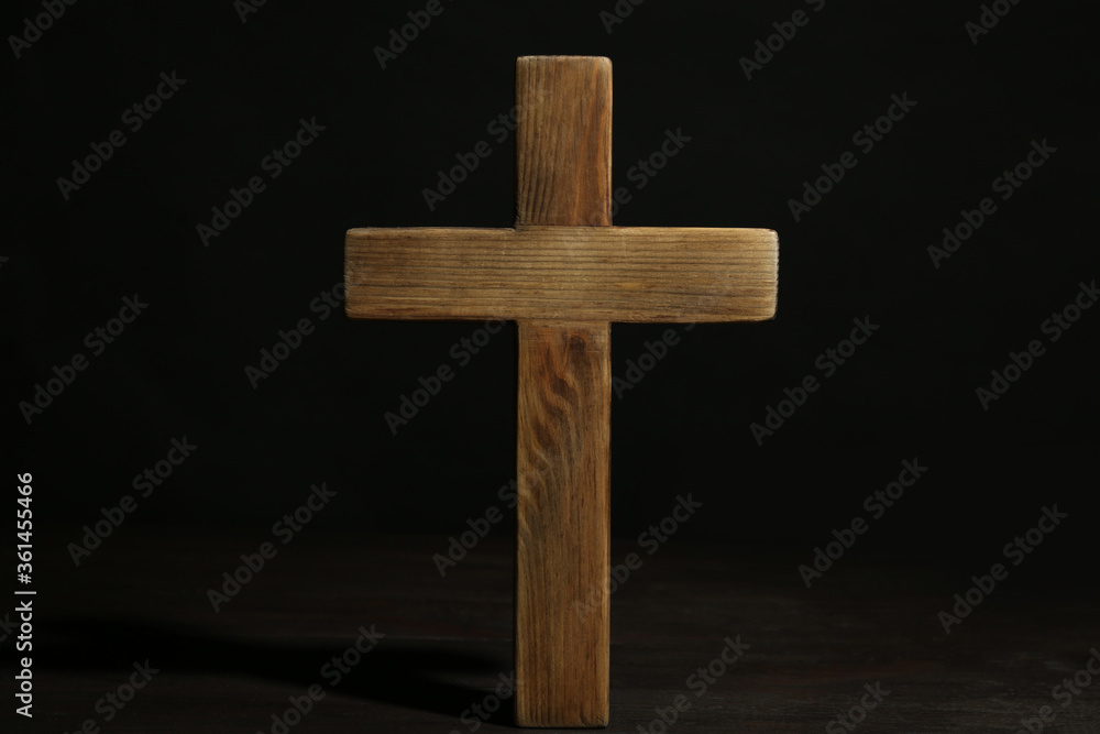 Christian cross on wooden table against black background. Religion concept