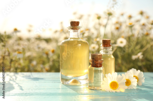 Bottles of chamomile essential oil on light blue wooden table in field