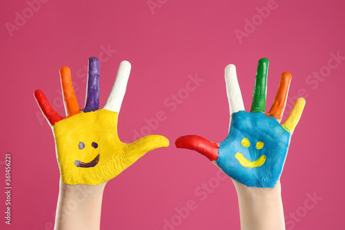 Kid with smiling faces drawn on palms against pink background, closeup