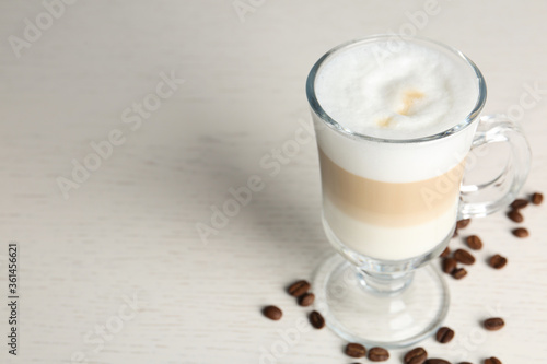 Delicious latte macchiato and coffee beans on white table, space for text