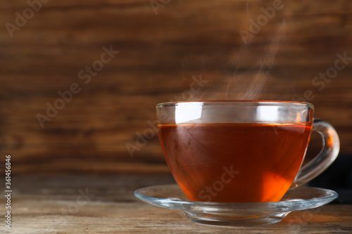 Cup of tasty black tea on wooden table. Space for text
