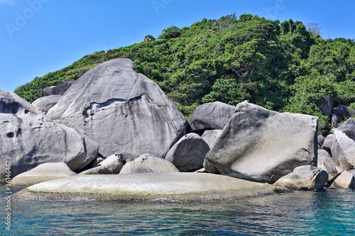 Amazing Similan island. On the shores of the turquoise sea lie huge ancient smooth boulders. Behind them rises a hill overgrown with dense tropical forest. Bright blue sky, sunny day. Thailand.