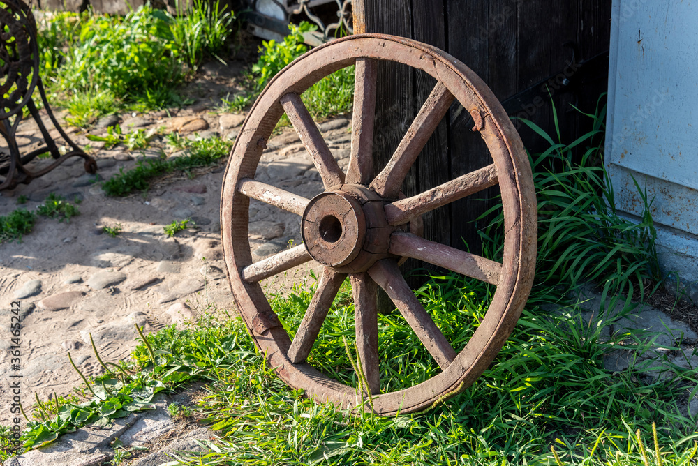 Ancient wooden wheel of a cart near the door of a rural barn.