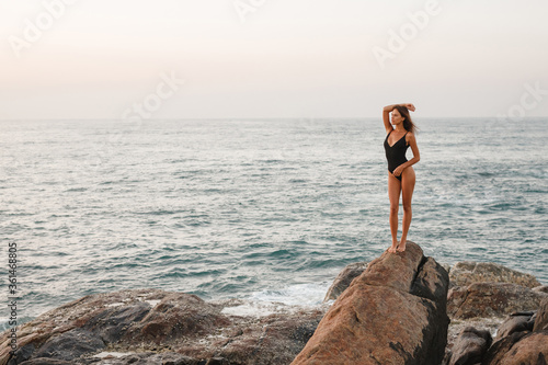 Beautiful blonde woman stand on a rock by the sea. The style of summer holiday. Enjoy summer vacation by the sea