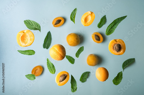 Ripe apricot slices and mint leaves are flying above blue surface Flat lay with tasty apricots on mint background