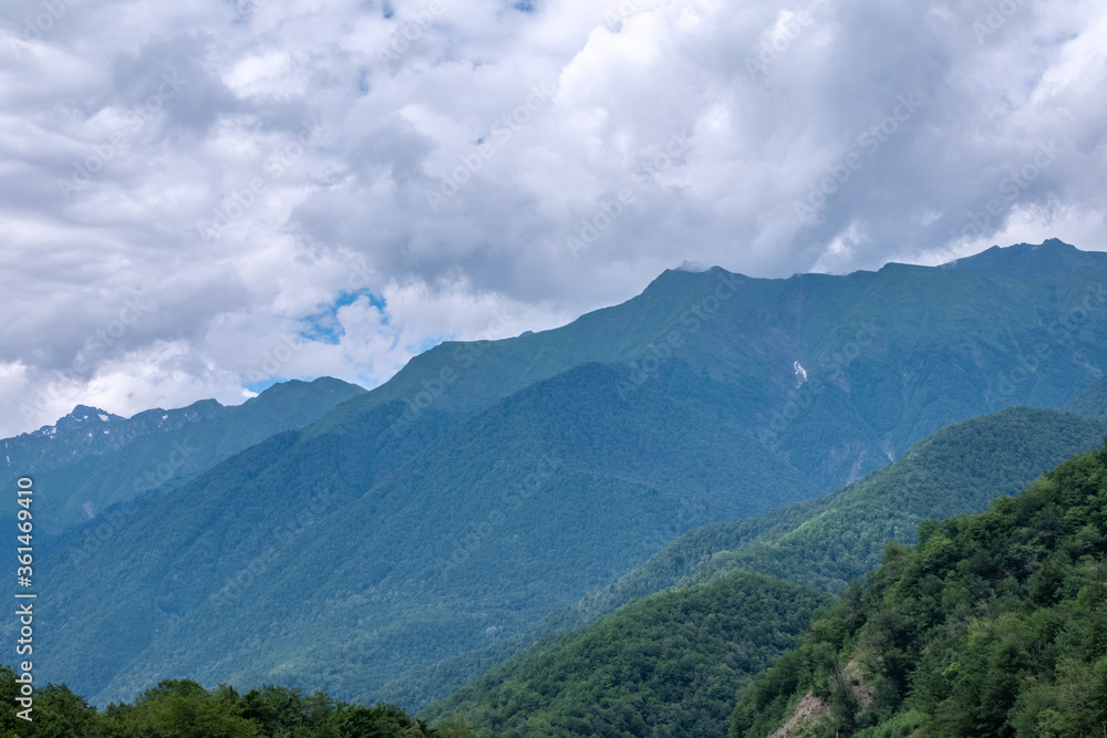 High green mountains with snowy peaks in clouds and fog