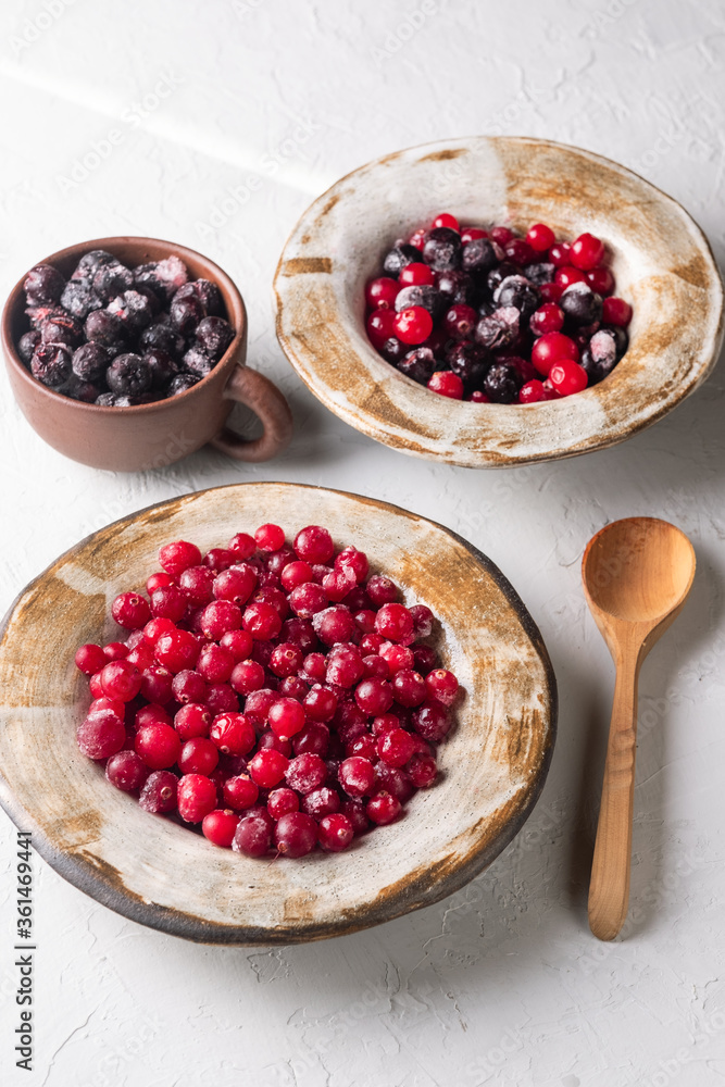 frozen cranberries and chokeberries in clay dishes on a light background frozen cranberries and chokeberries in clay dishes on a light background