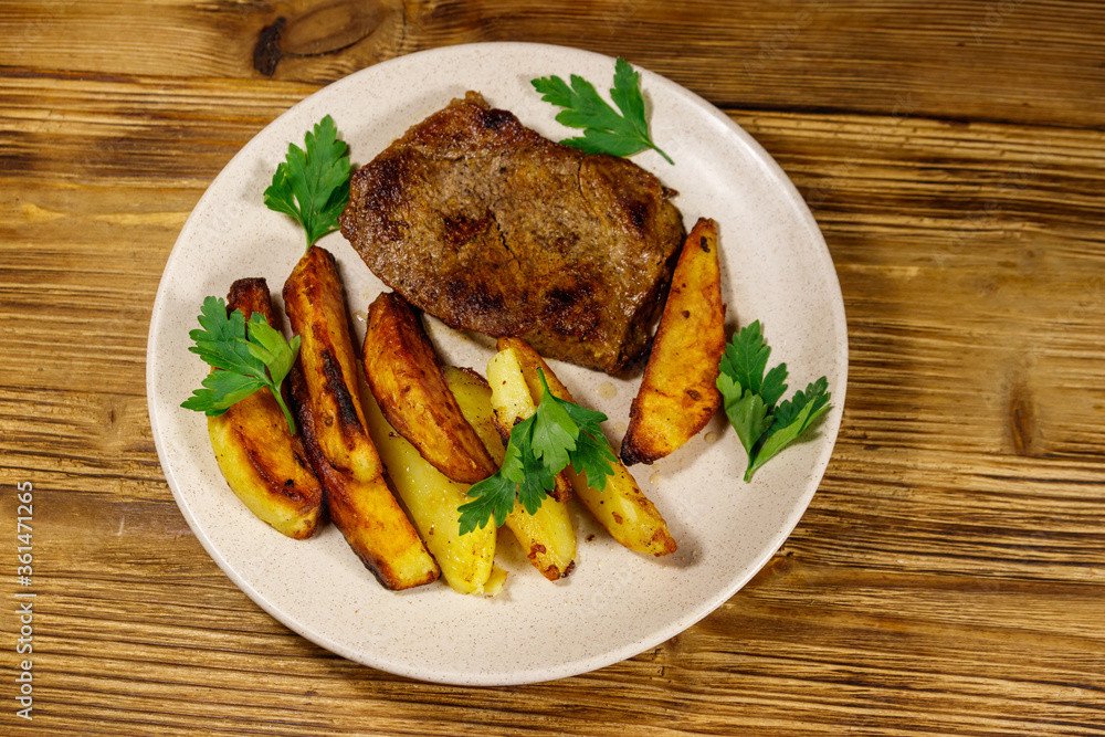 Fried beef steak with potato wedges on wooden table. Top view Fried beef steak with potato wedges on wooden table. Top view