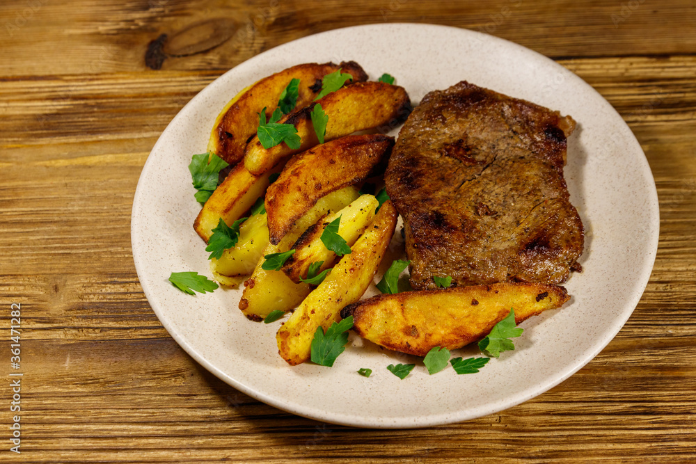 Fried beef steak with potato wedges on wooden table Fried beef steak with potato wedges on wooden table