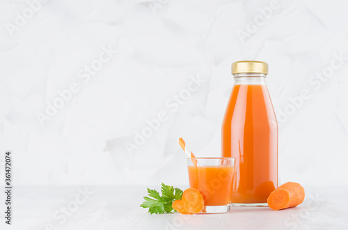 Foto Fresh vegetable orange carrot juice in glass bottle mock up with glass, straw, green parsley, slices in soft light white interior on wood table