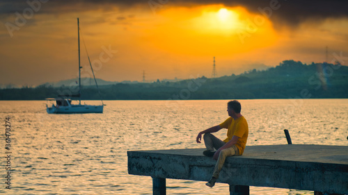 A man in yellow on the pier meditate at sunset
