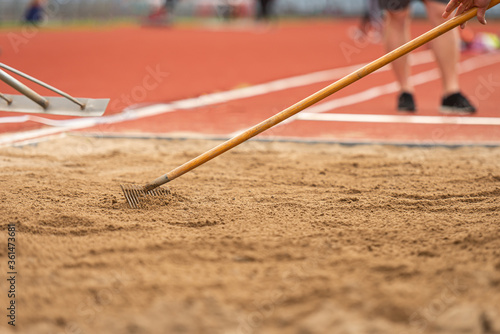 A volunteer raking the sand pit for the next jump on a long jump competition photo