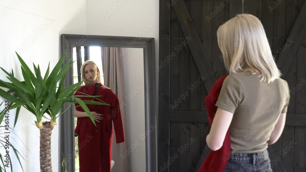 blonde girl chooses is dressing up a red coat for autumn season at mirror at home blonde girl chooses is dressing up a red coat for autumn season at mirror at home