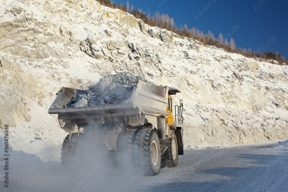 Heavy mining dump truck transports ore stone in the quarry mining enterprise, close-up. Mining industry. Heavy mining dump truck transports ore stone in the quarry mining enterprise, close-up. Mining industry.